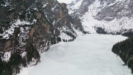 aerial view over frozen braies lake with snow capped mountains in background in trentino, italy - drone shot