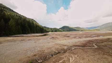 Low-FPV-aerial-over-dried-up-expanse-Stave-Lake-showcasing-rugged-rocks-dust-laden-fallen-logs,-tree-stumps-bright-sunny-day-with-wispy-clouds-in-the-sky-Beautiful-exciting-adventurous-terrain