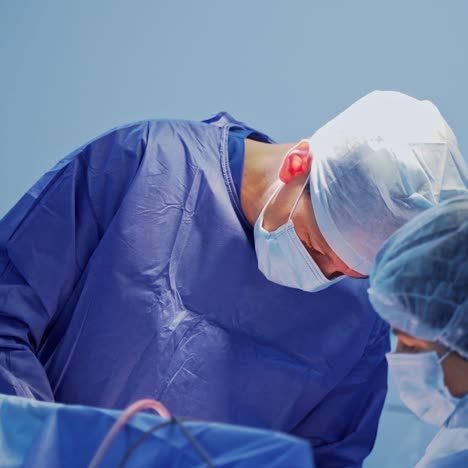 doctor and nurse in the surgical room. professional neurosurgeon and female assistant in blue medical uniform and mask conduct a surgery.