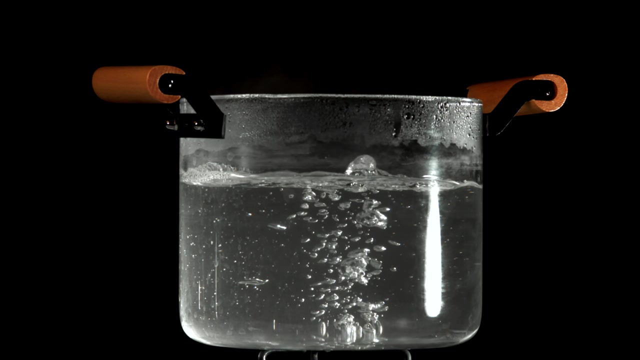 Acqua che bolle in una pentola di vetro trasparente su sfondo nero