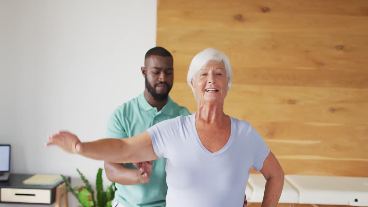 Video of happy african american male physiotherapist examining caucasian senior woman