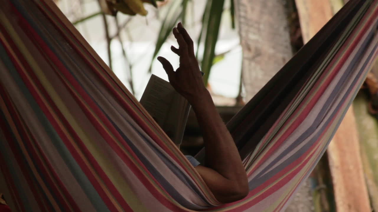 In a hammock a man reads aloud — peace and poetry by the ocean.