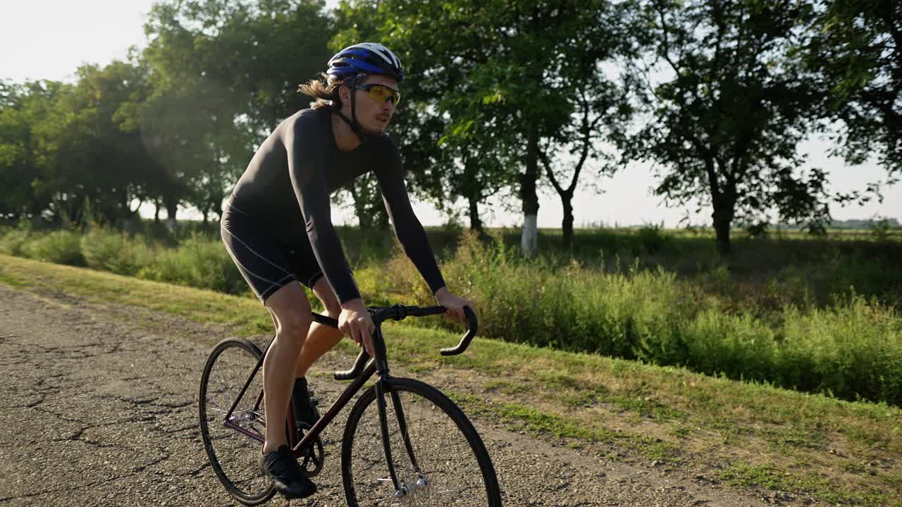 Giovane ciclista con casco pedala lungo la strada asfaltata, vista laterale.