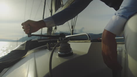 sailor operating yacht winch at sunset