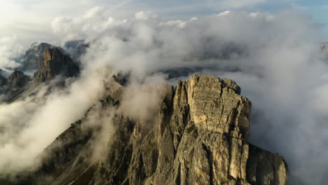 Flying-around-rocky-mountain-tops-in-middle-of-low-hanging-clouds-in-Dolomites,-Italy---Aerial-view