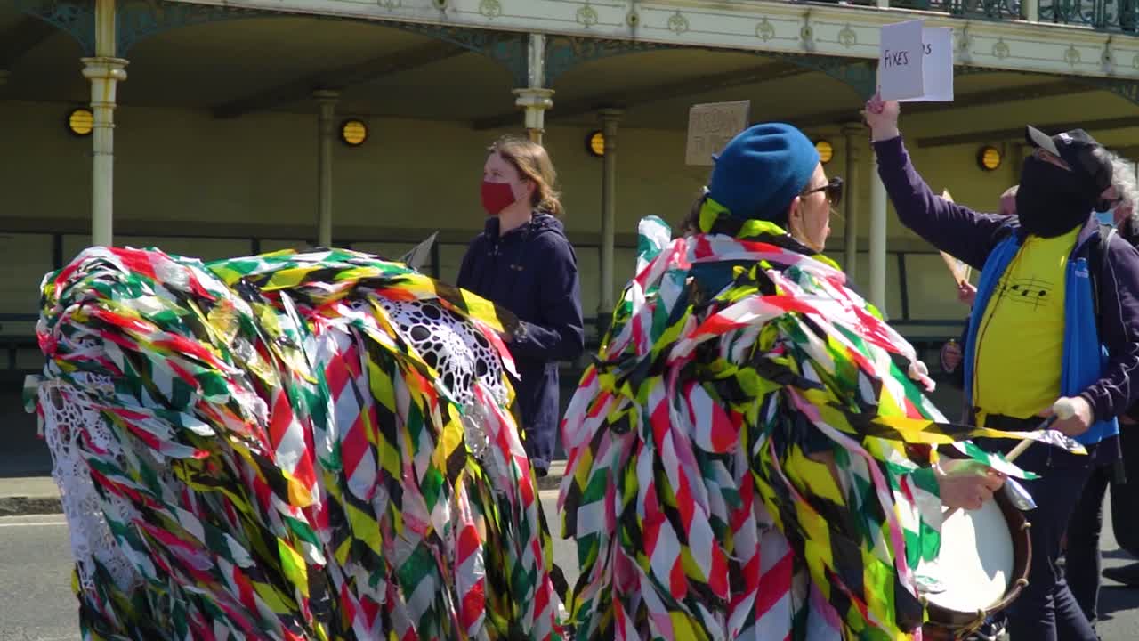 Energetic costume wearing protestants playing drums on a road peacefully standing up for their rights bright sunny day holding cards and signs in their hands