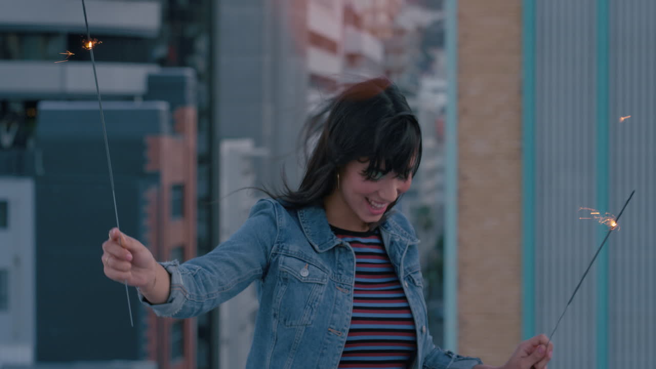 feliz joven asiática sosteniendo bengalas bailando en la azotea por la noche celebrando la víspera de año nuevo disfrutando de la celebración navideña