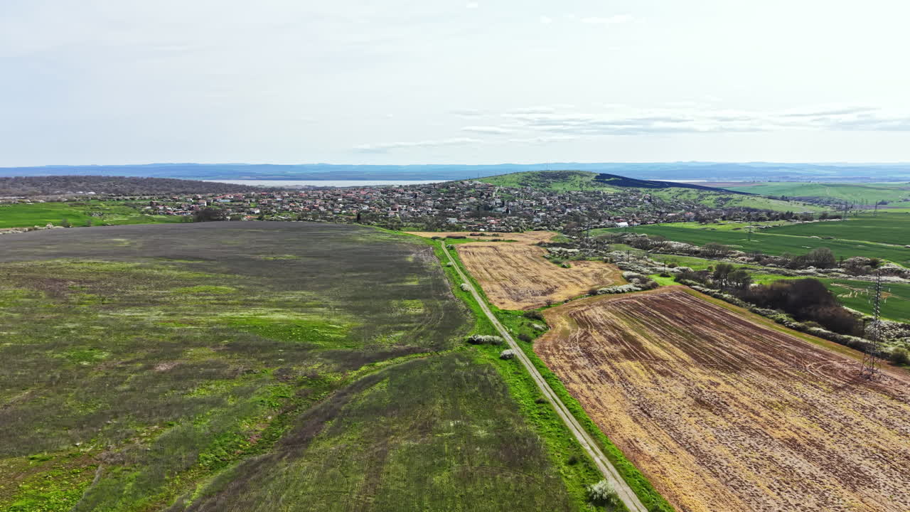 Canais de água com aspecto de pergaminho estendem-se pelos campos em paisagem rural perto de colinas com vegetação esparsa e terras agrícolas durante o dia claro.