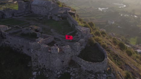 Albanian-flag-on-top-of-Schloss-Shkodra-during-sunrise,-aerial