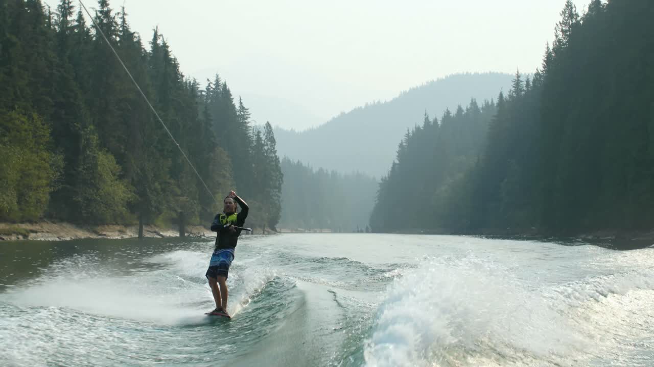 vista frontal de un joven caucásico haciendo trucos en wakeboard en el río de la ciudad 4k