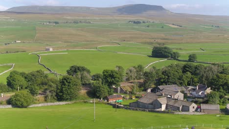 Drone-footage-on-a-sunny-summer-day-in-the-village-of-Selside,-North-Yorkshire-moving-sideways-over-farmland-and-fields,-dry-stone-walls-with-Pen-Y-Ghent-mountain-in-the-distance