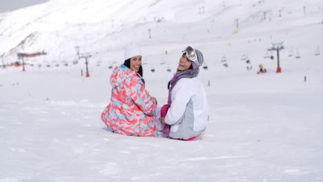 Two-young-women-sitting-in-snow-at-a-ski-resort