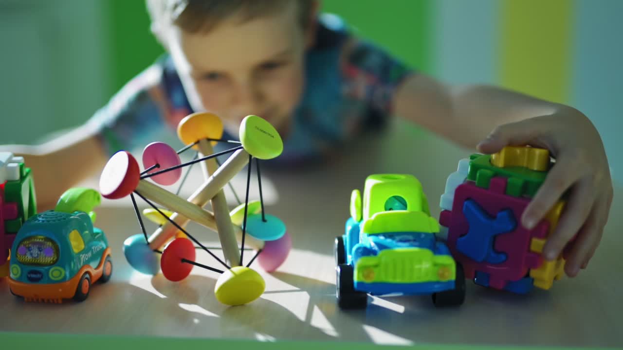Colorful toys on the table. Little boy captures toys together in the room. Satisfied child with many toys. Close-up. Slow motion.
