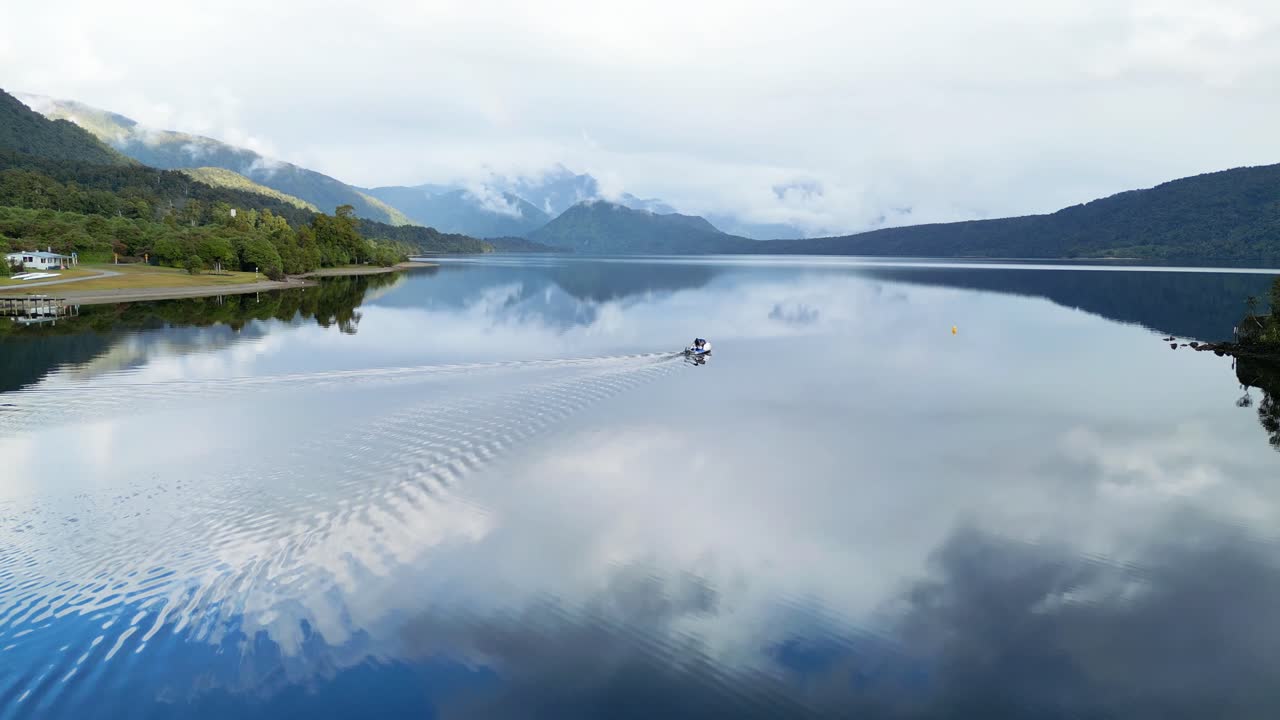 A boat cruises out onto glassy, calm Lake Kaniere, West Coast, New Zealand.