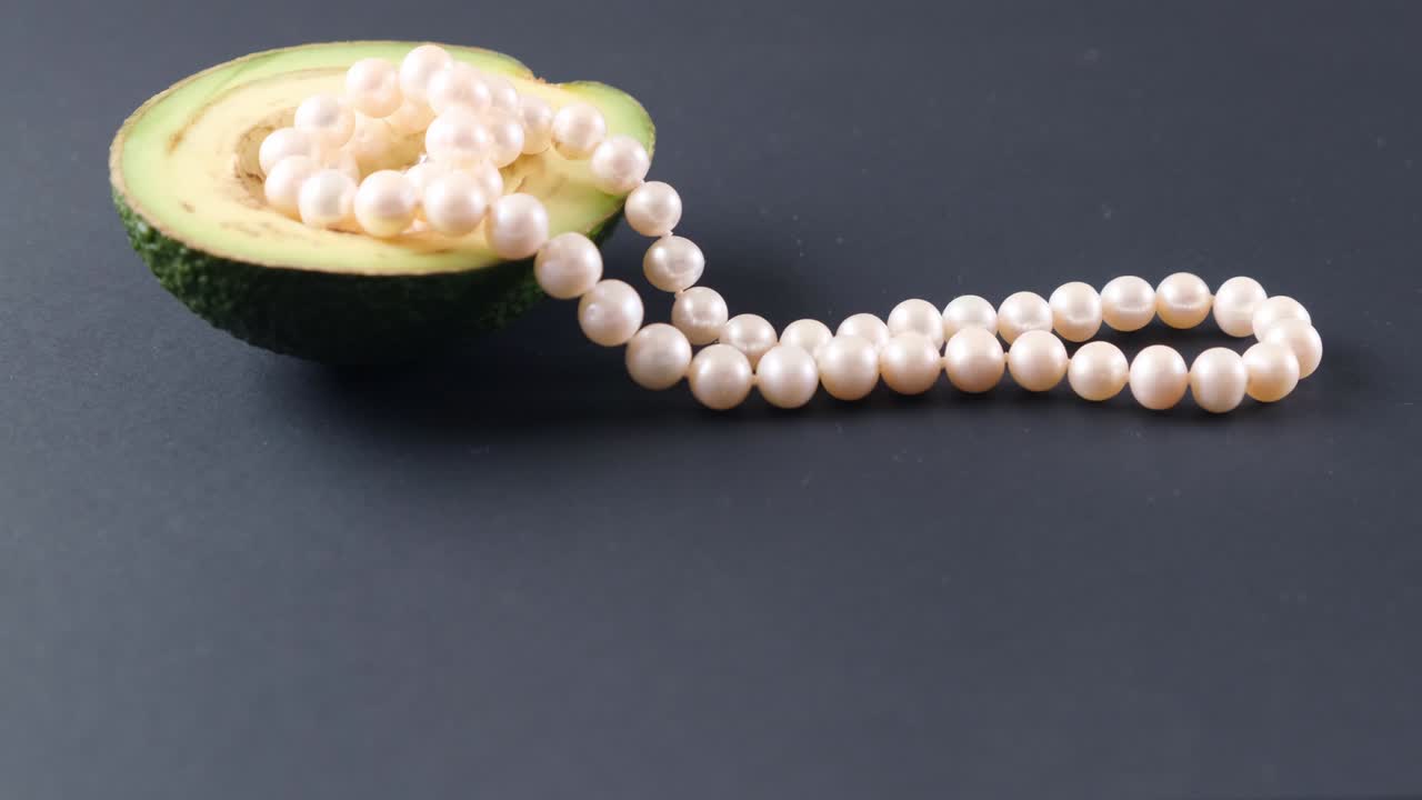la mitad de un aguacate con perlas en un fondo negro. surrealismo. diseño de alimentos de moda
