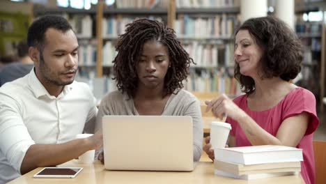 gente pensativa hablando mientras usa una laptop en la biblioteca