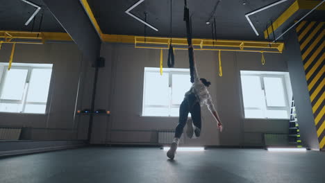 sportswoman is training alone in gym rotating on suspension using modern trx system for workout