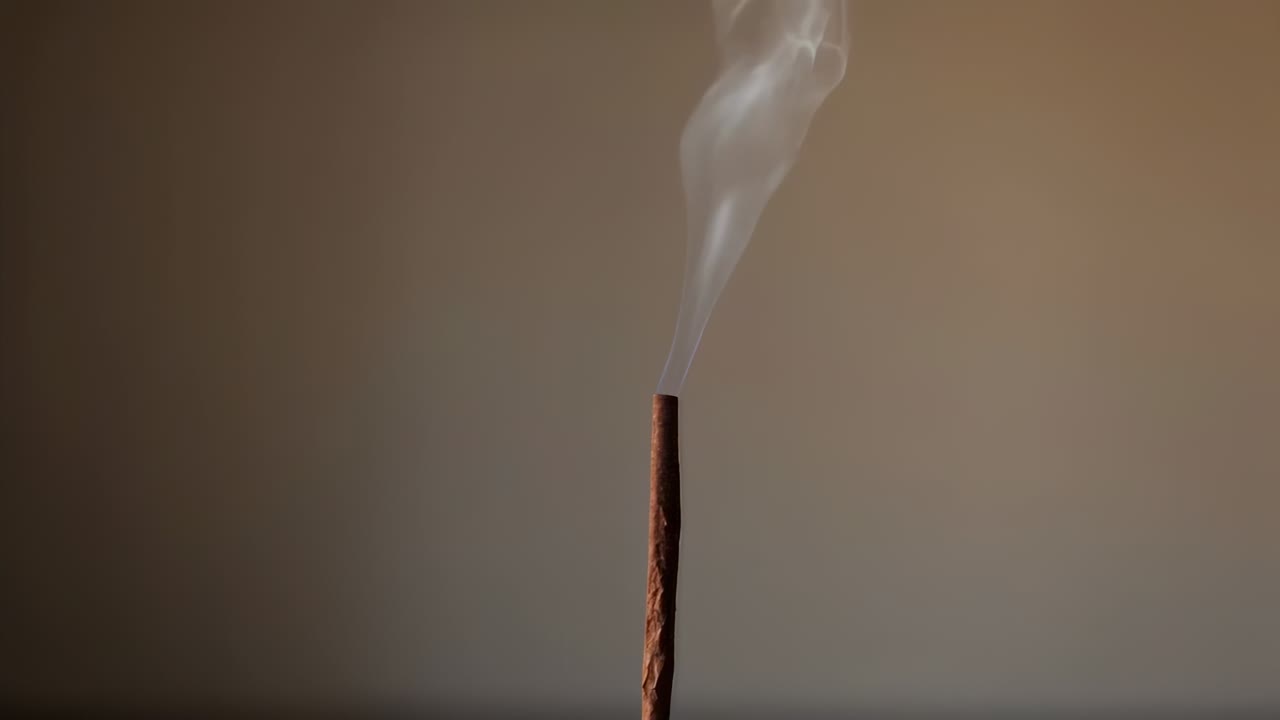 Charred tip releasing smoke, single incense stick sending curling plumes in room near tabletop