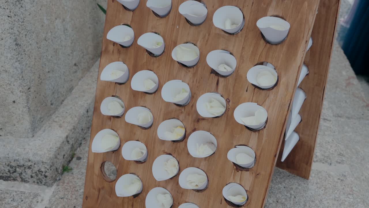 Wooden display board holding paper cones filled with petals, set up for an outdoor event.