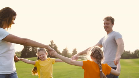 Happy-Parents-And-Little-Daughters-Holding-Hands-And-Spinning-Around-On-Green-Grass-Field-In-The-Park-2