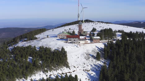 aerial shot ascending over snow covered hill showing broadcasting tower, wind turbine and buildings