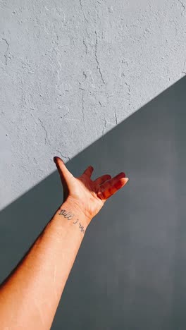mano alcanzando contra una pared texturizada a la luz del sol