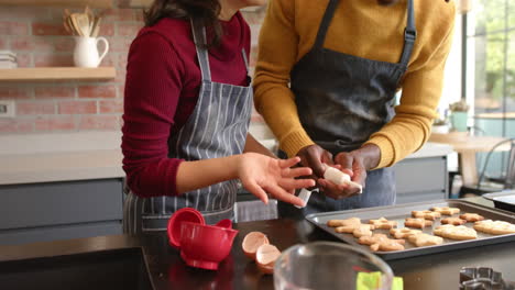 una pareja feliz en delantales decorando galletas de navidad en la cocina, en cámara lenta.