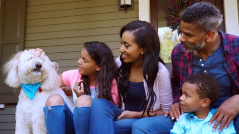 family with children and pet dog sit on steps of home