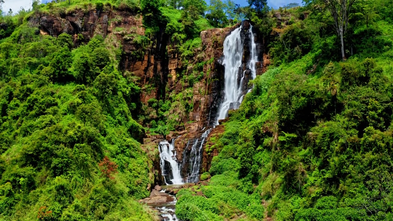 Aerial drone view of a waterfall in Ella, Sri Lanka surrounded by lush jungle, mountains and tropical green landscapes.