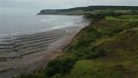 Establishing-Aerial-Drone-Shot-Along-North-Yorkshire-Coast-in-Mist-at-Low-Tide-Near-Robin-Hood's-Bay