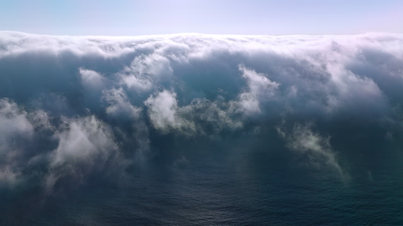 Blue ocean water covering with thick fog. Bright sun shining on the top of hazy cloudscape. Aerial view.