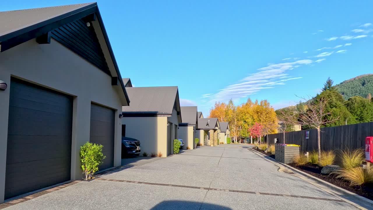 Vehicle moves along quiet suburban road lined with modern houses, autumn trees, clear blue sky