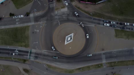 aerial drone top rotating shot over a road crossing in rosario, argentina during evening time with cars from all sides passing by on the sides of a white boat statue