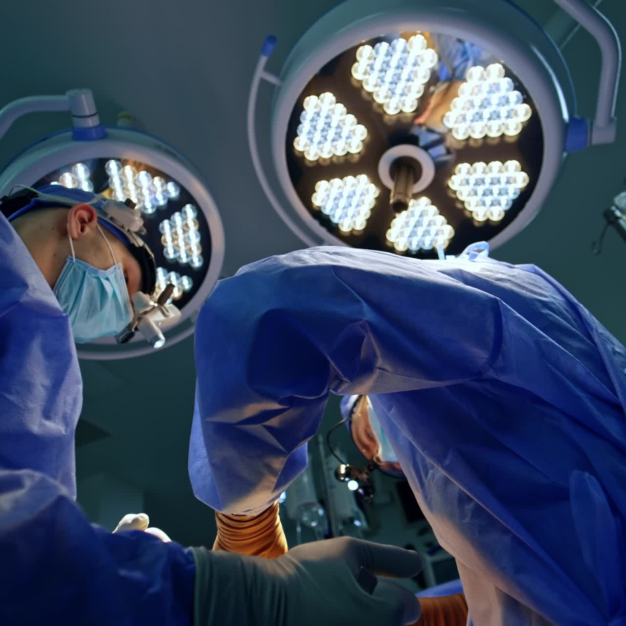 Male neurosurgeons carrying out the operation. Doctors operate under the modern illumination equipment. Low angle view