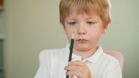 serious toddler boy studies green crayon pencil in hands