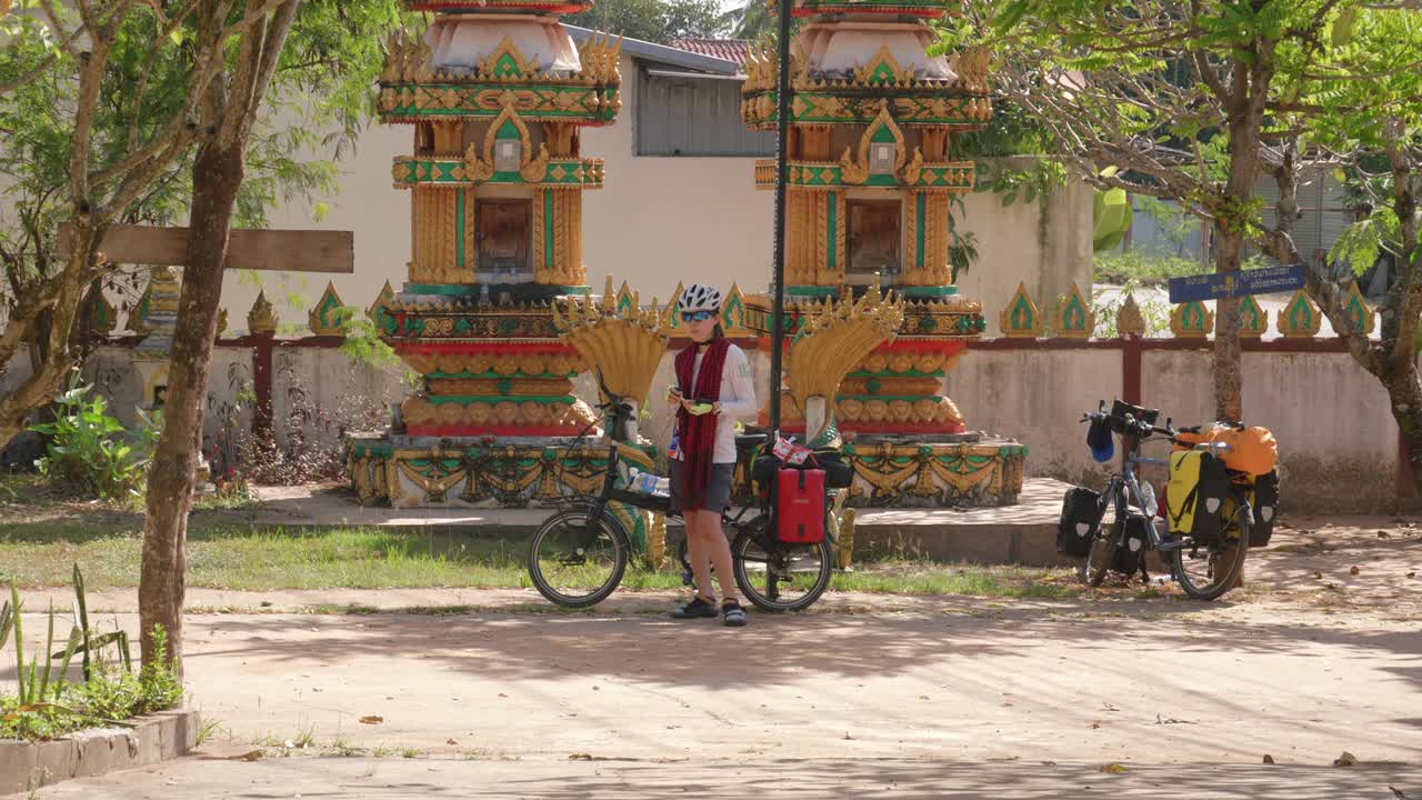 Young Asian cyclist woman resting having lunch at a temple on the street in Laos
