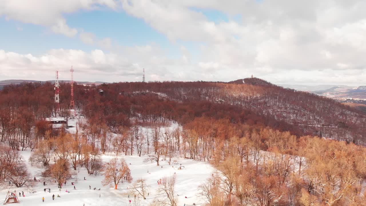 Aerial pan following a drone flying over a beautiful winter land with snowy hills, forest and a city in the background