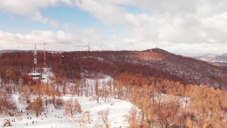 aerial pan following a drone flying over a beautiful winter land with snowy hills, forest and a city in the background
