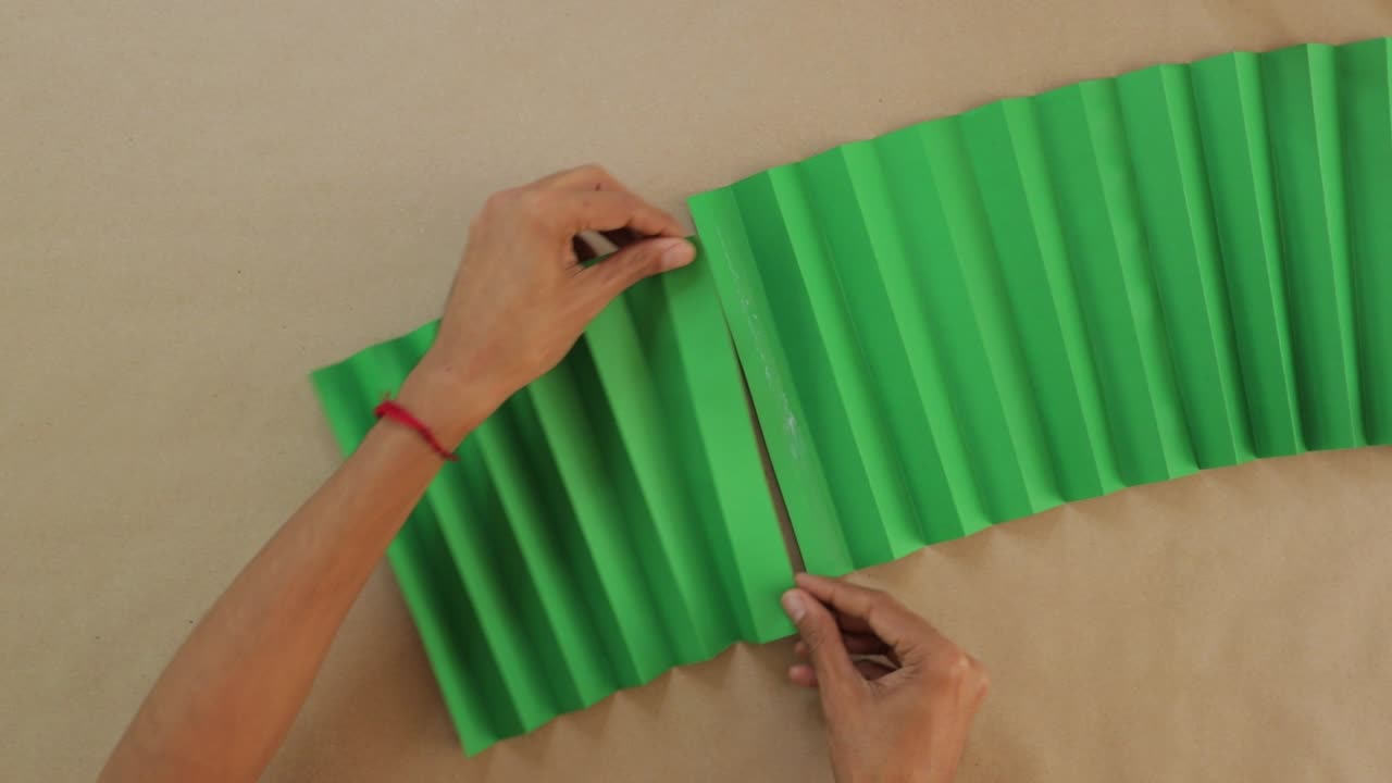 hombre trabaja con papel verde en zigzag, pegando para el abanico tradicional mexicano