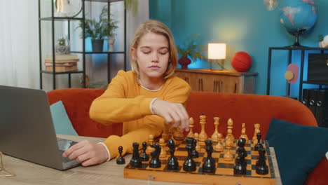 teenager boy playing online chess on laptop with real chessboard thoughtfully moving pieces at table