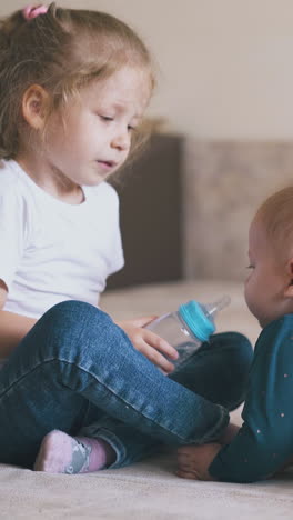 funny girl sucks teat on water bottle and gives to cute little baby brother but mother takes away in spacious room