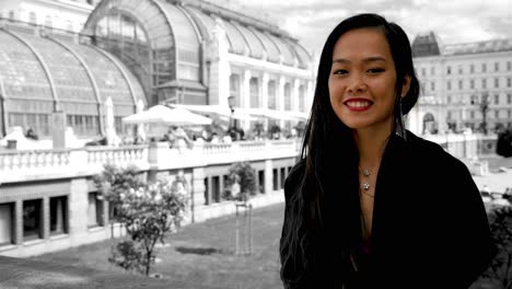 Asian-woman-smiling-in-front-of-Vienna's-Palmenhaus-in-Burggarten,-black-and-white-background-with-color-pop-effect