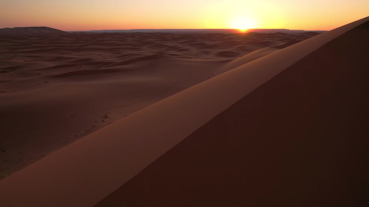 L'alba illumina il mare di dune dell'Erg Chebbi vicino a Merzouga, Marocco, rivelando infinite formazioni scolpite dal vento e texture sabbiose fluide attraverso il Sahara, ripresa aerea con drone in avanzamento lento.