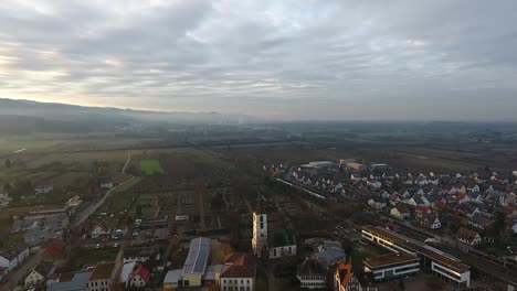 Vista-De-Una-Iglesia-Con-Un-Cementerio-Al-Fondo,-Un-Tren-Circula-Por-Una-Vía-Férrea