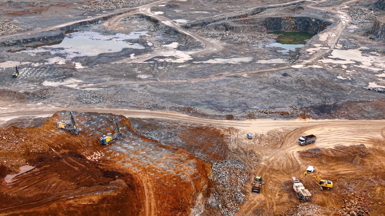 Mining equipment and drilling rigs on rock ledge in quarry. Aerial shot of heavy machinery, drilling rigs, and excavators operating on different levels of a mine