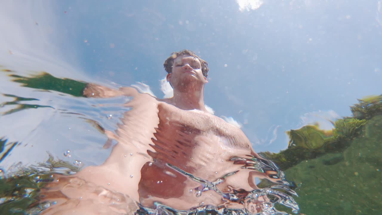 selfie psicodélico del joven blanco bajo el agua bajo el sol, cámara lenta