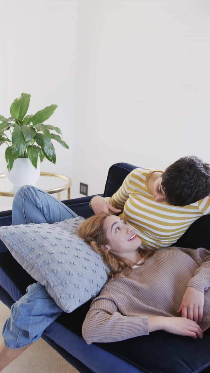 Happy caucasian lesbian couple lying on sofa and talking in sunny living room