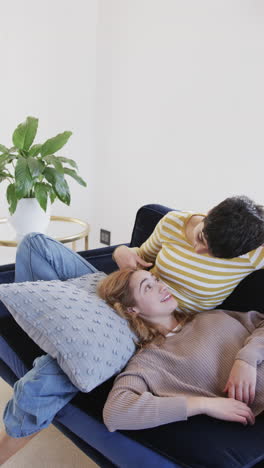 happy caucasian lesbian couple lying on sofa and talking in sunny living room