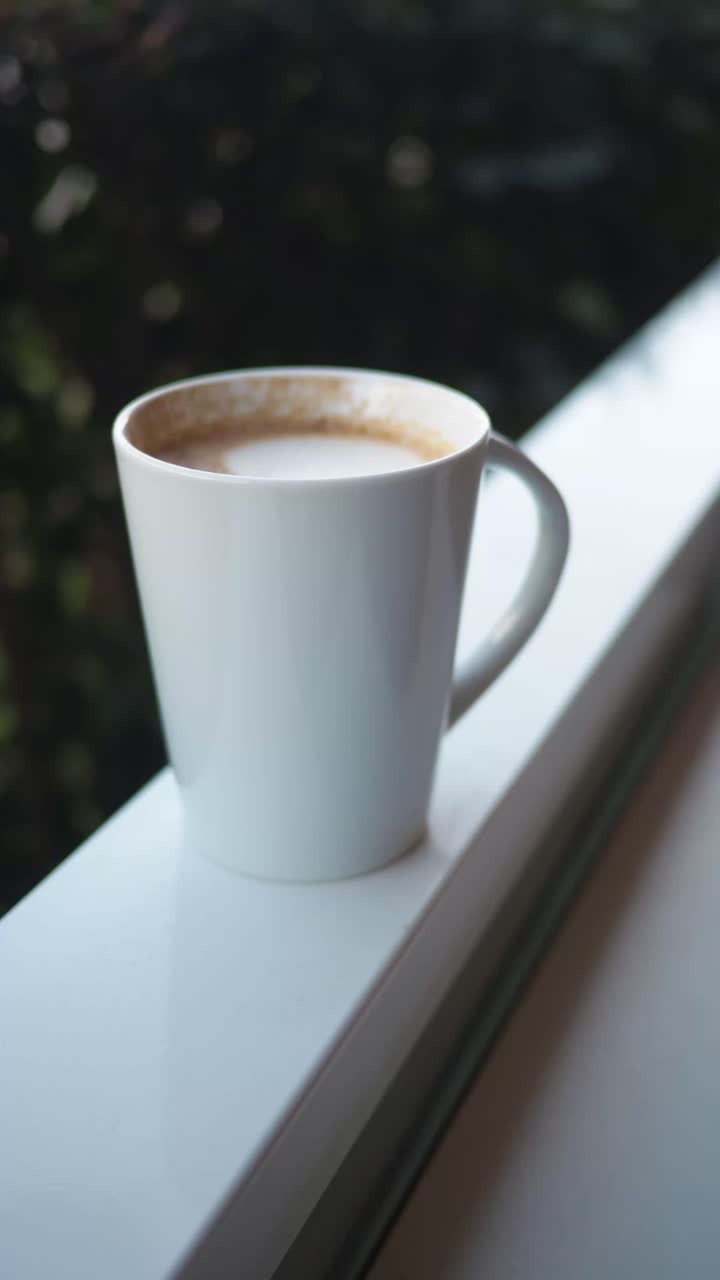 Mano che prende una tazza da caffè bianca dal parapetto del balcone