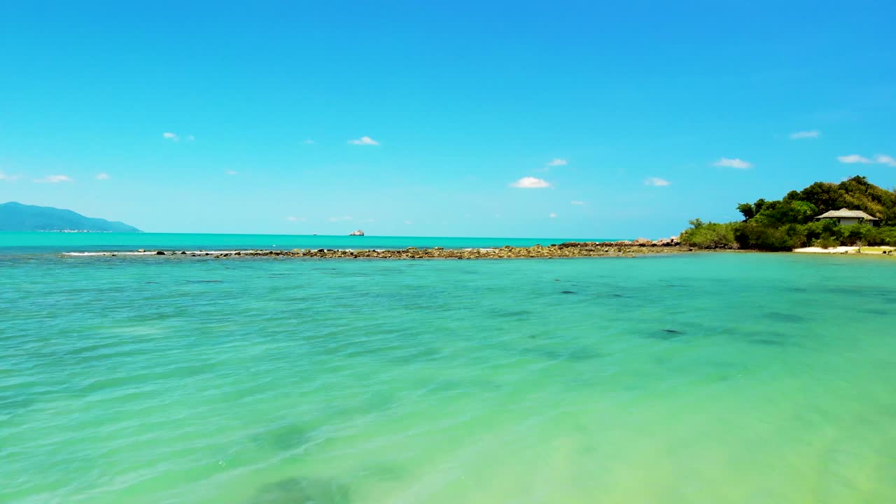 A fast zipline aerial drone shot of Choeng Mon beach, with its crystal blue waters, white sandy beach, and a rocky coast, in the island of Koh Samui in Surat Thani province in Thailand